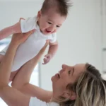 Mother holds baby up in the air. Both are smiling.