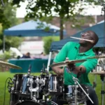 Drummer Plays Outdoors with Drumstick in Mouth